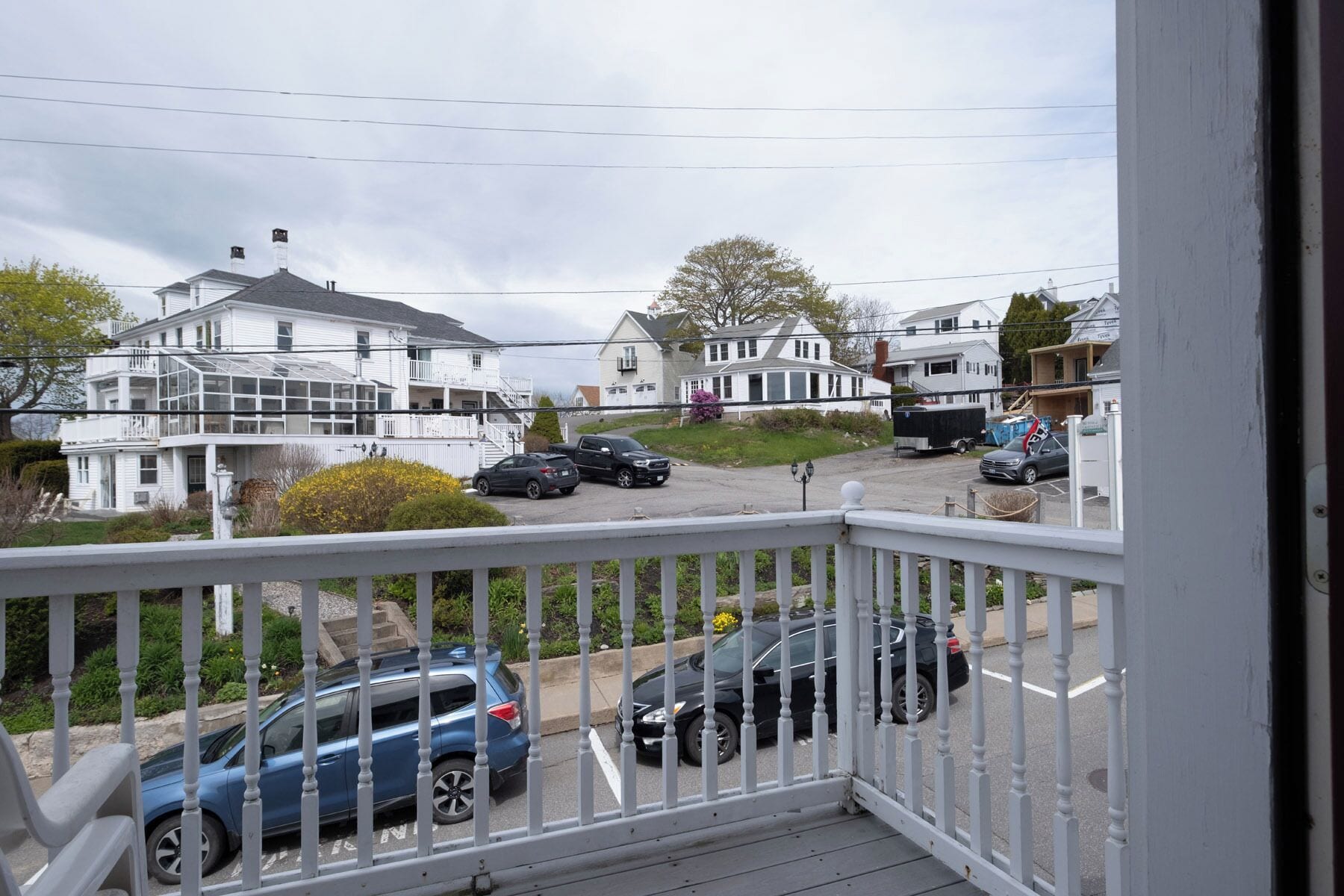A residential street with houses, parked cars, and a white fence.