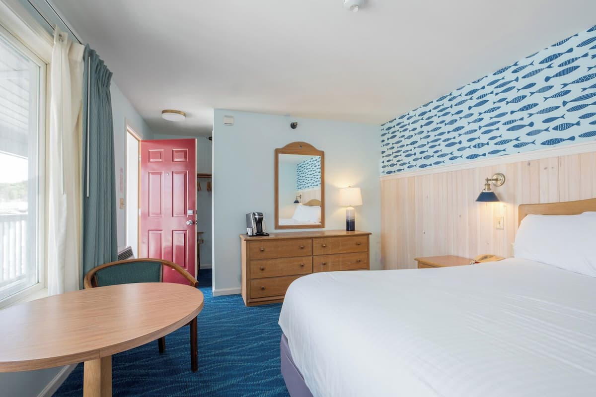 A hotel room with a bed, a desk, a chair, a dresser, and a mirror.