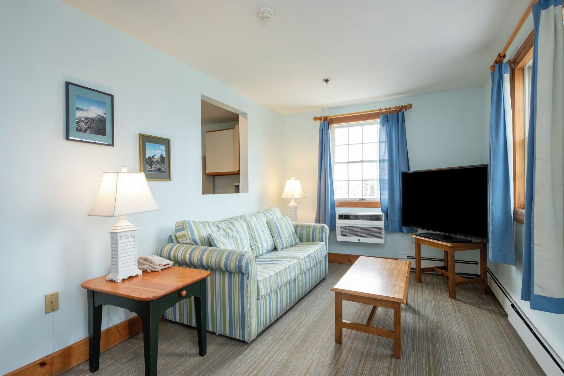 A room with a striped sofa, a small wooden table, a TV, and a window with curtains.