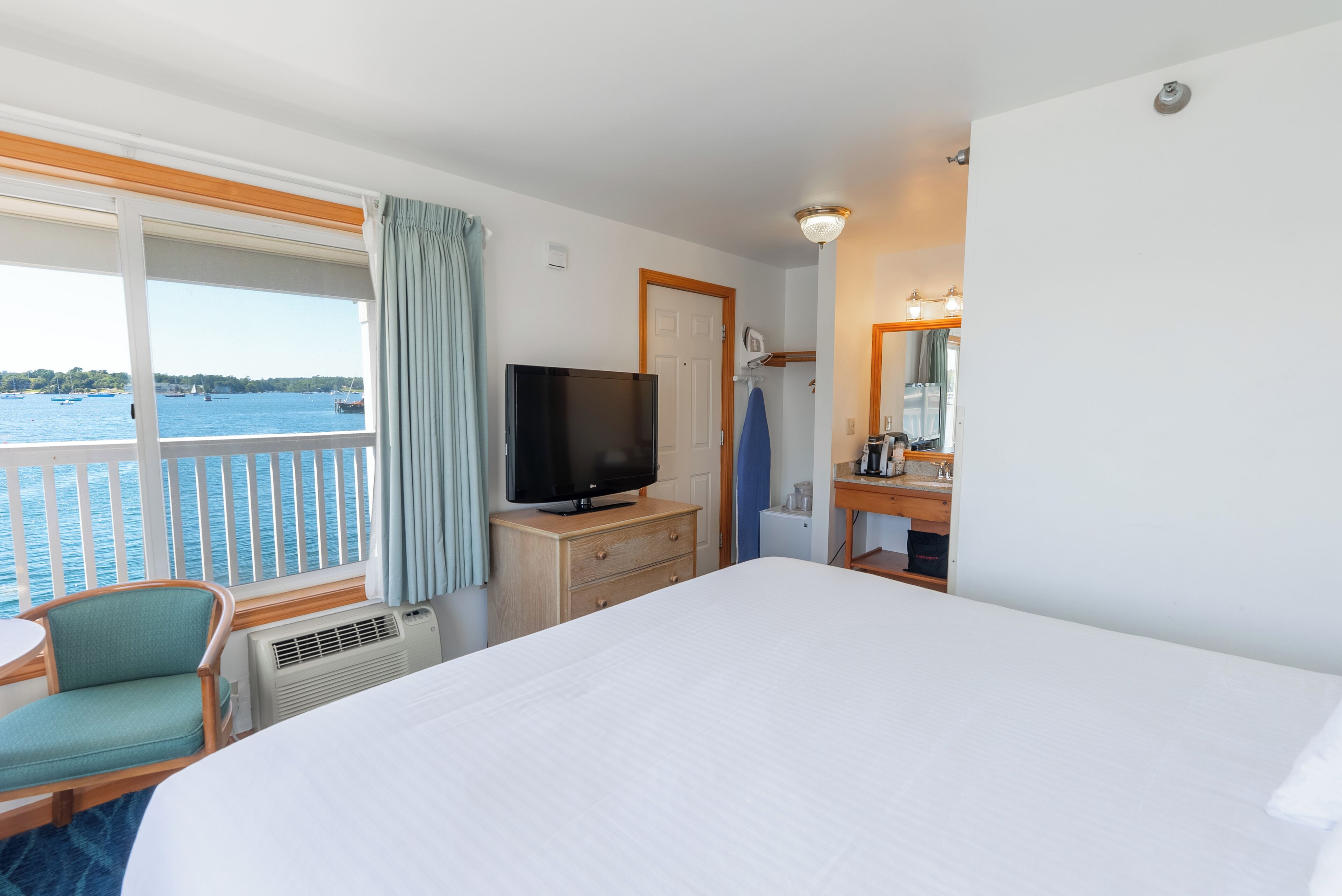 A hotel room with a large bed, a television, a desk with a mirror, and a view of the sea.