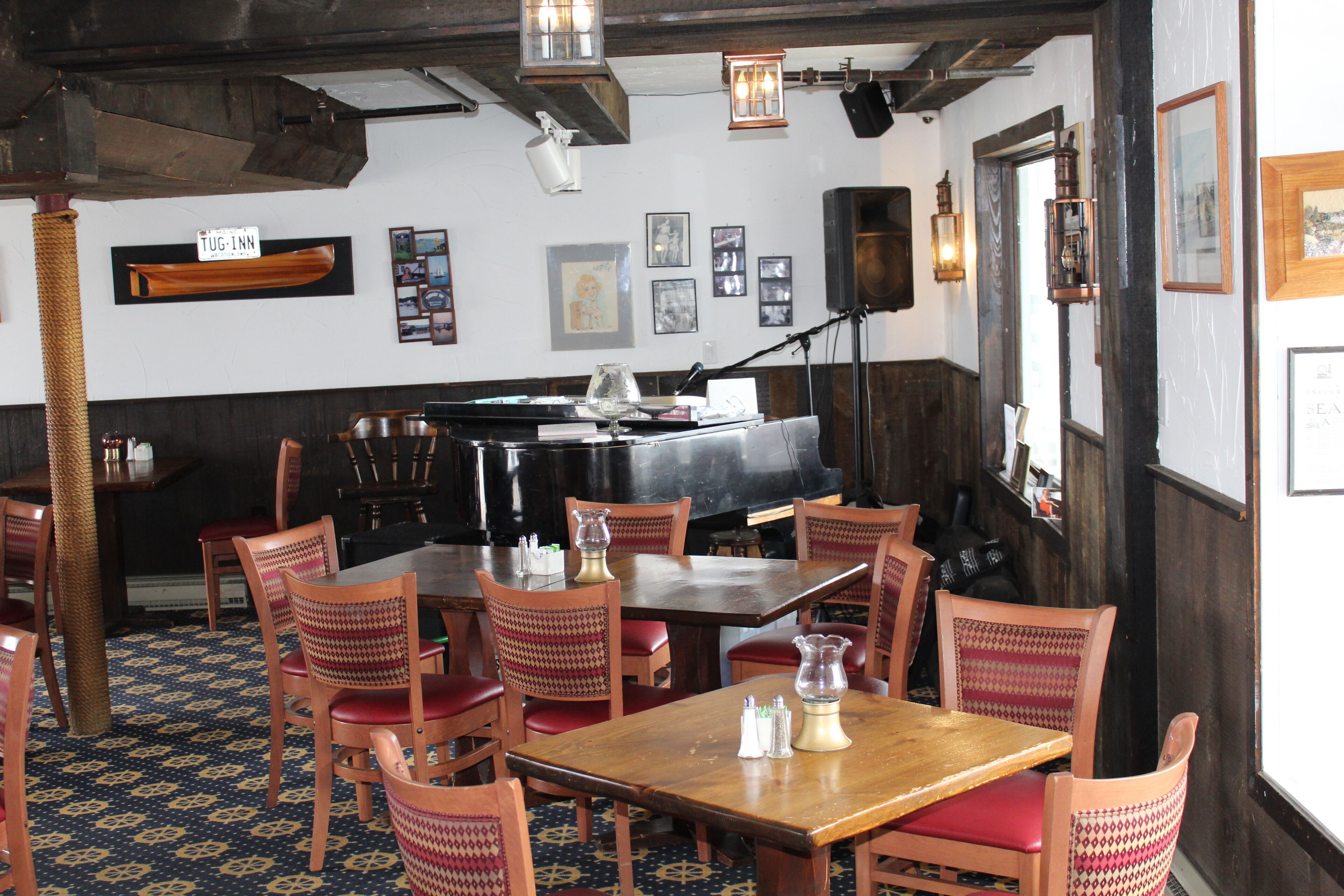 Um restaurante com mesas e cadeiras de madeira, um piano e quadros nas paredes.
