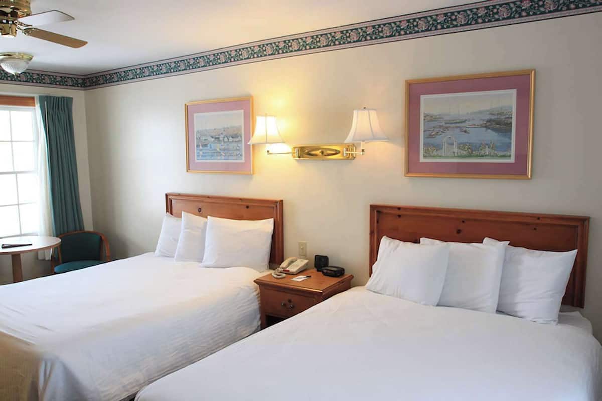 A hotel room with two beds, a nightstand with a phone and a lamp, a chair, and a window with curtains.