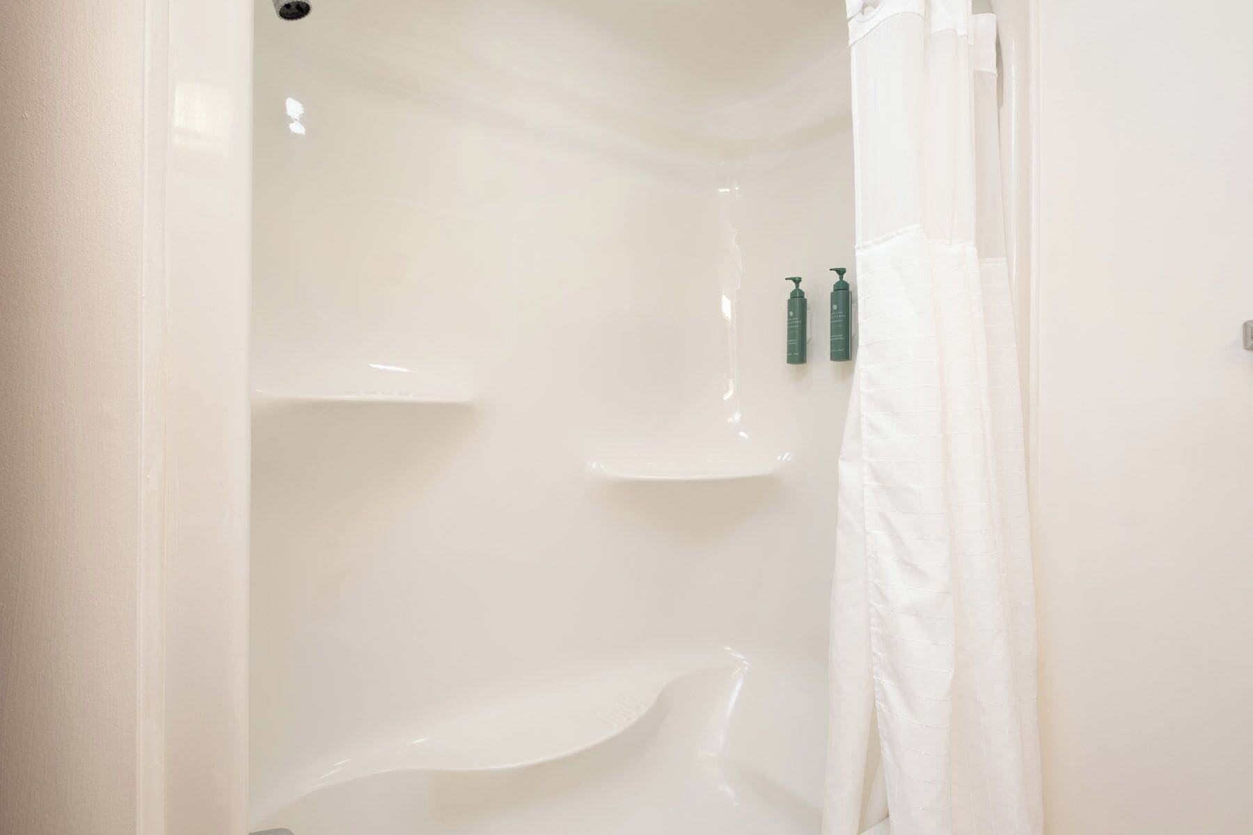 A white bathroom with a bathtub, a shower curtain, and two green bottles on the wall.