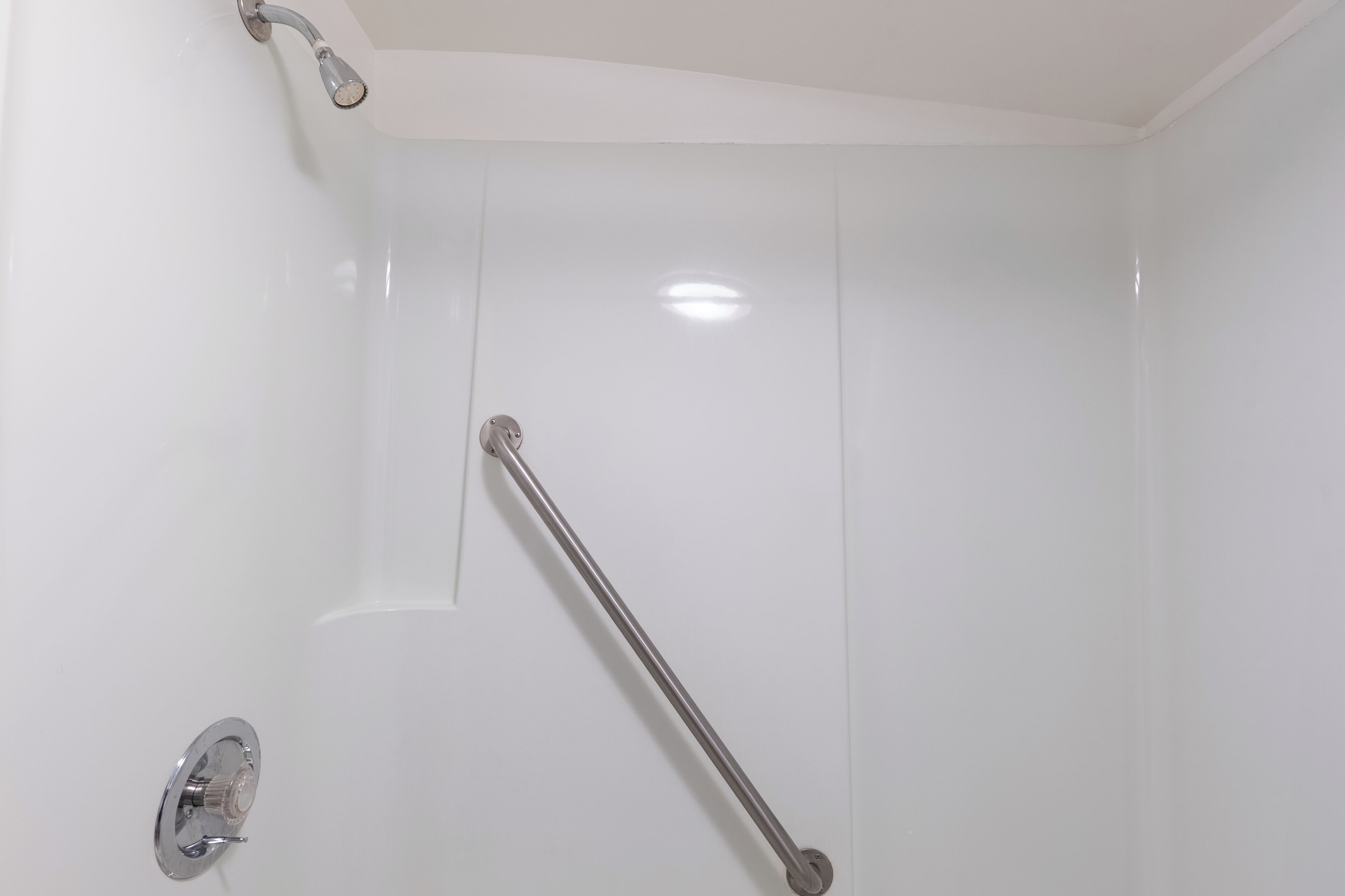 A bathroom with a white wall, a shower area, and a grab bar.