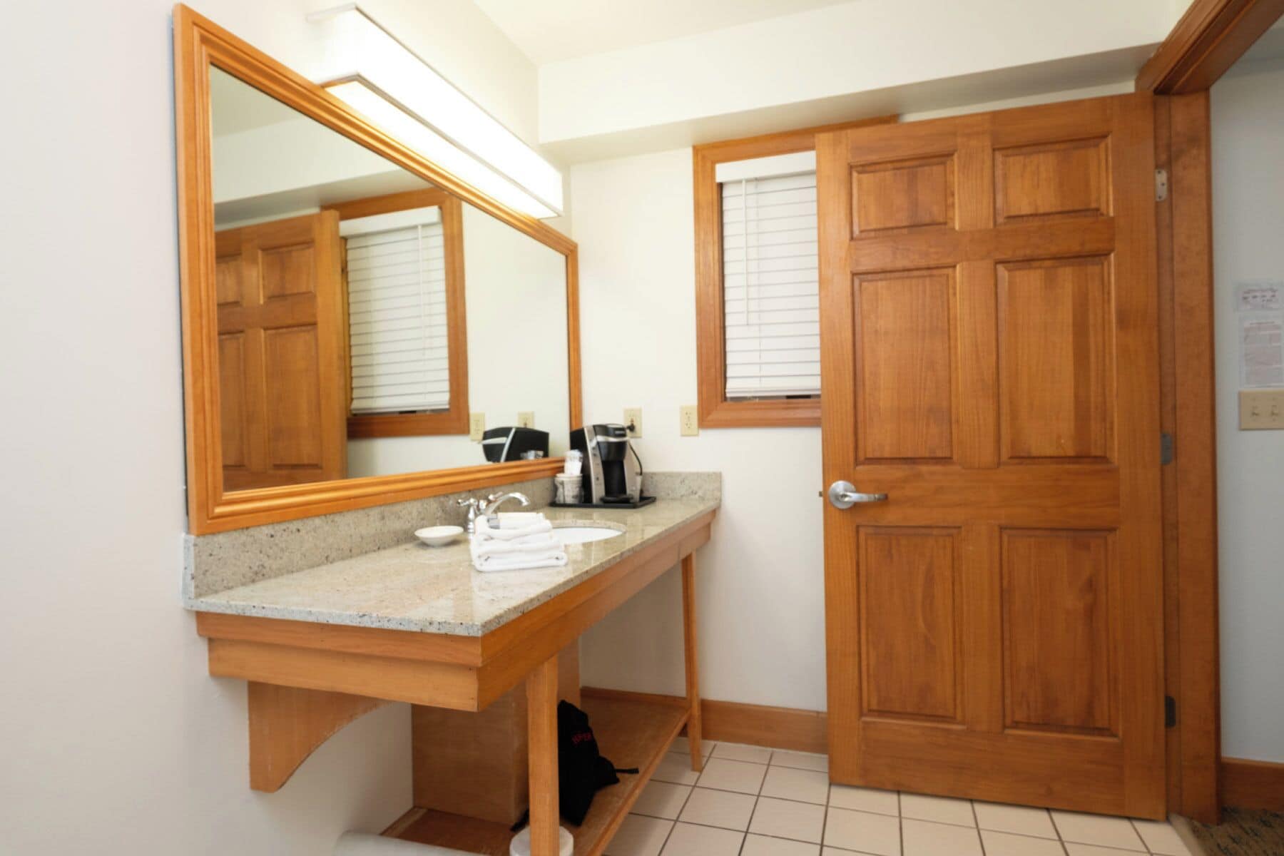 Une salle de bain avec un meuble-lavabo en bois, un évier, un miroir, une machine à café et une porte.