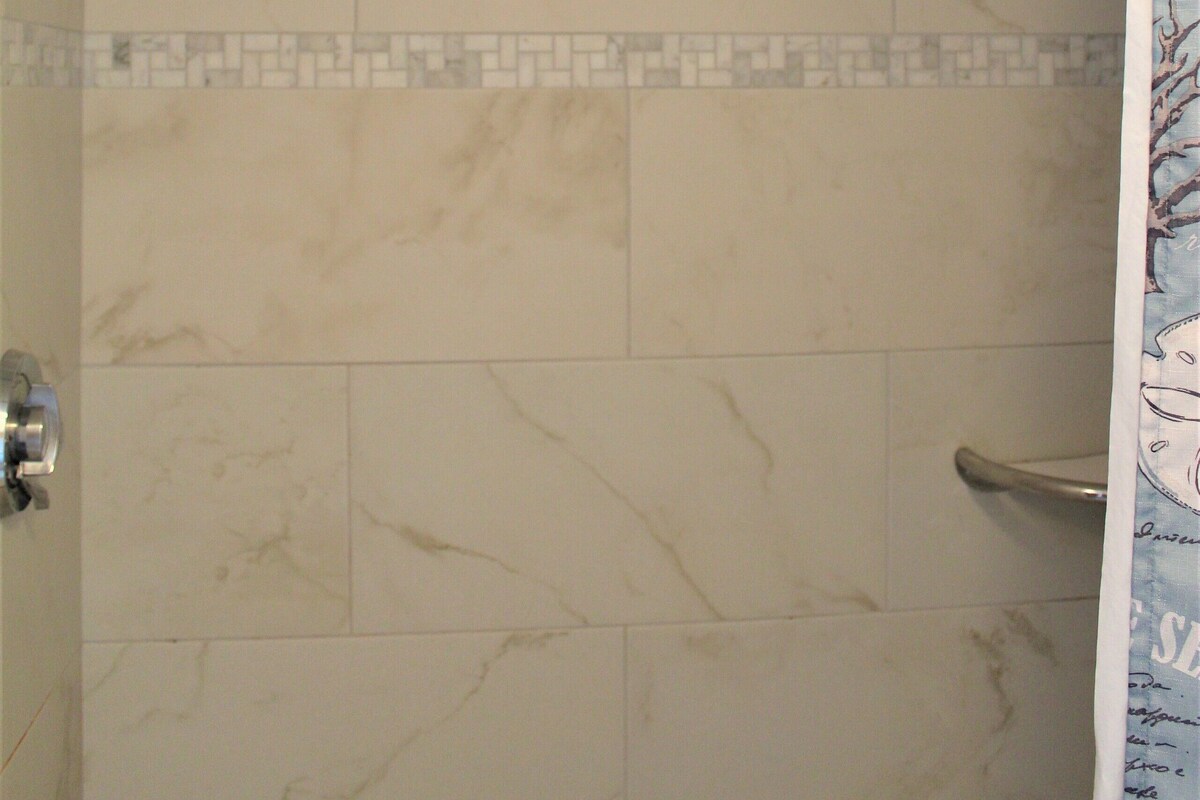 A shower with a glass door, a metal grab bar, and a tiled wall with a marble pattern.