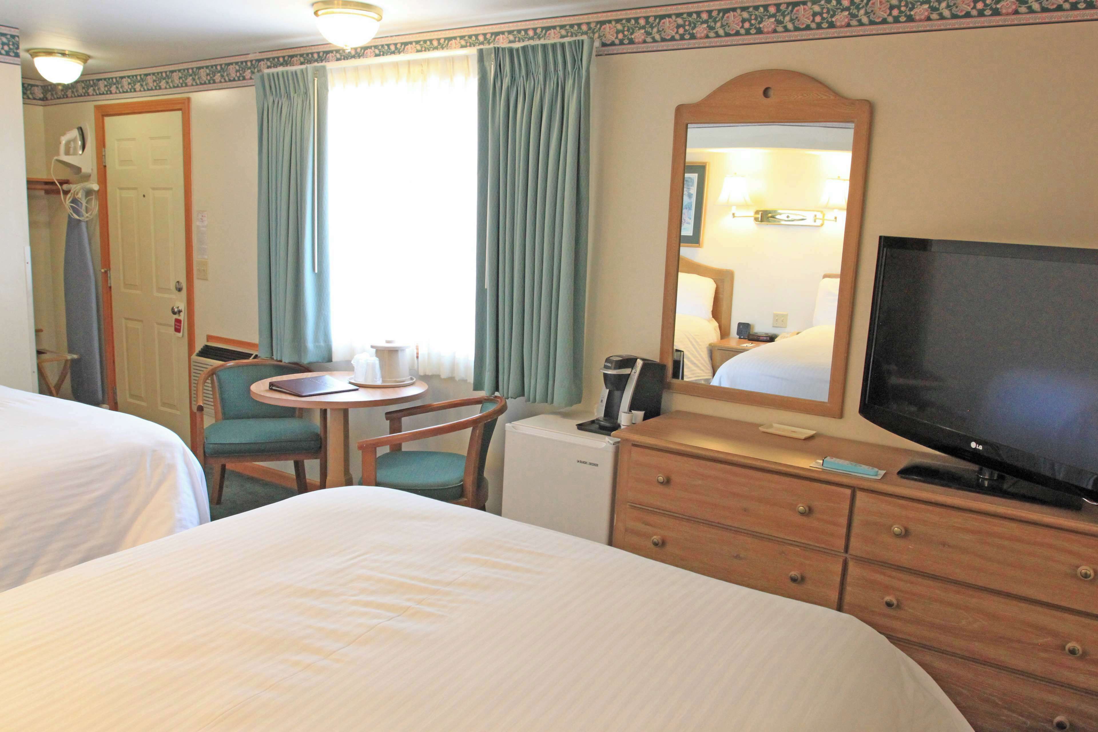 Een hotelkamer met twee bedden, een bureau, een stoel, een televisie en een spiegel.