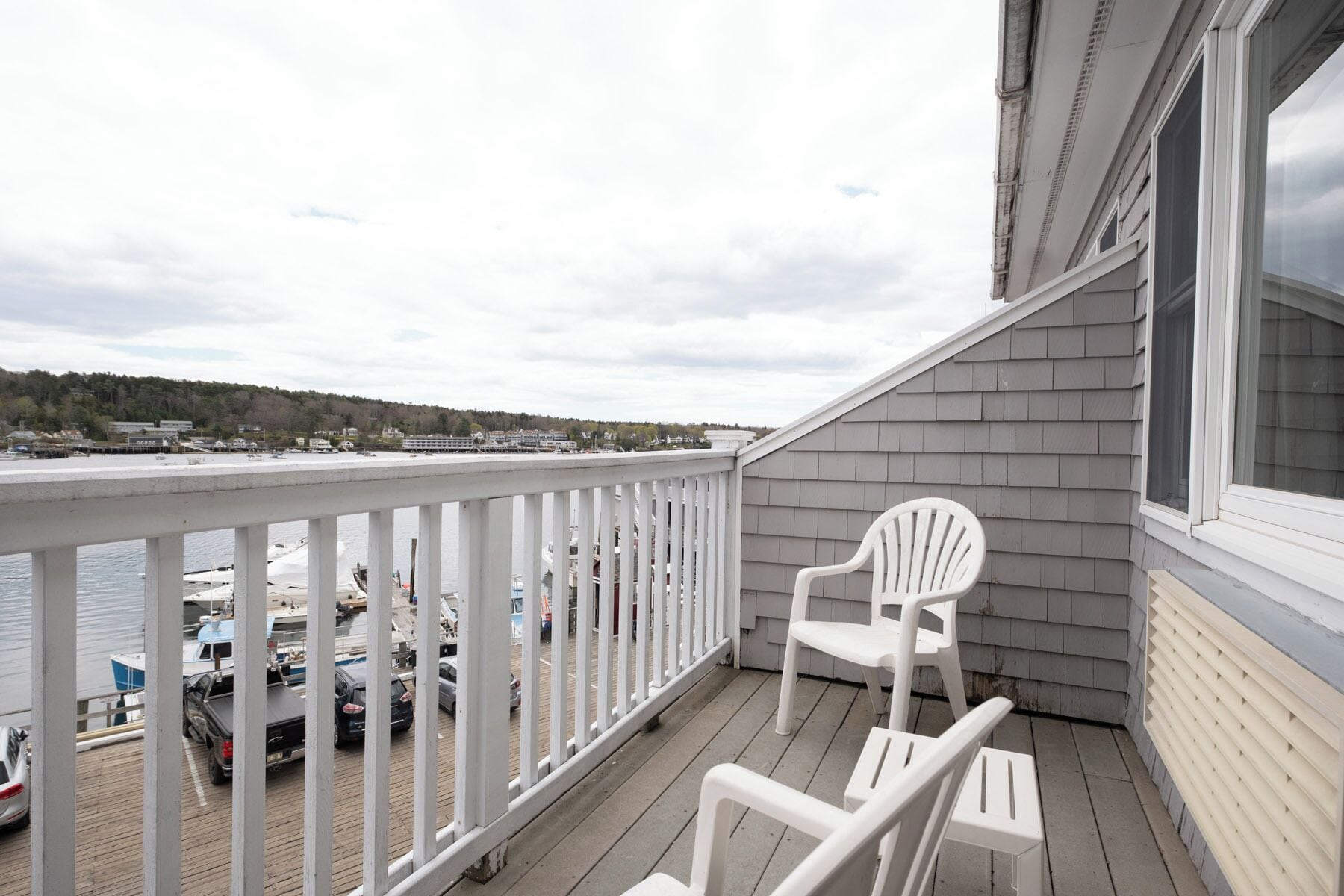 A balcony with a view of a marina, a white chair, and a wooden deck.