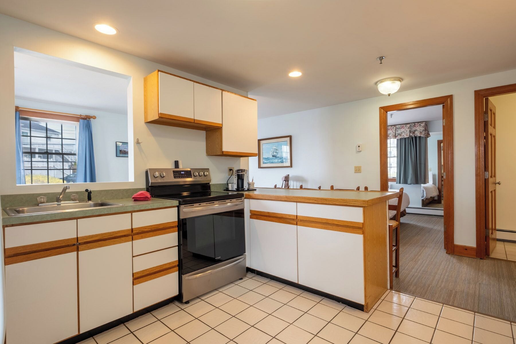 A compact kitchen with a stove, oven, and sink, wooden cabinets, and a small dining area.