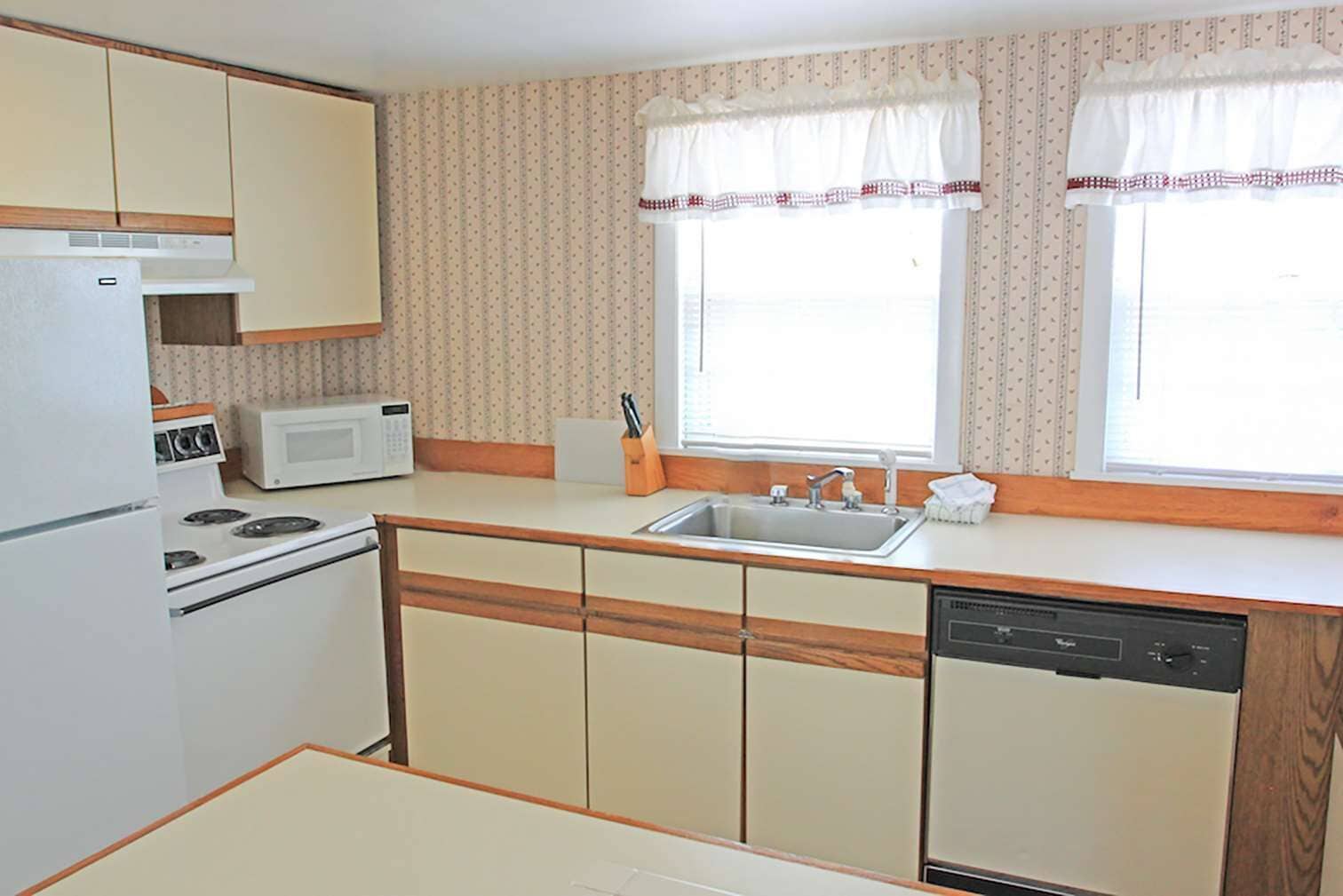 A compact kitchen with a stove, microwave, sink, and wooden cabinets.