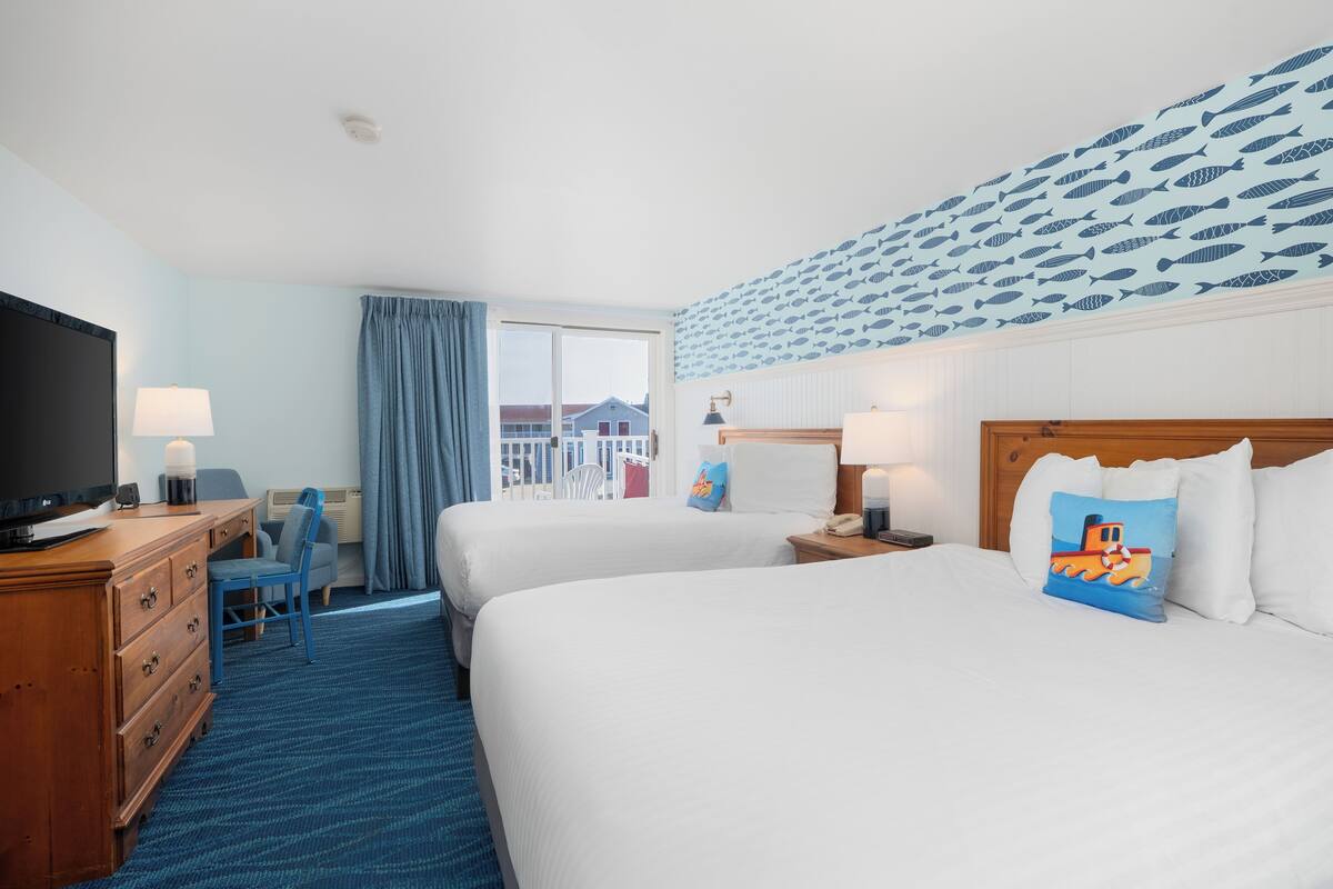 A hotel room with two beds, a desk with a TV, a chair, a window with curtains, and a wall with a fish pattern.