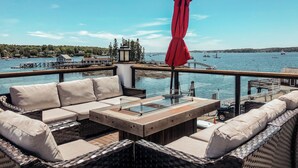 A waterfront patio with wicker furniture, a red umbrella, and a view of boats and a pier. - Tugboat Inn (Boothbay Harbor)