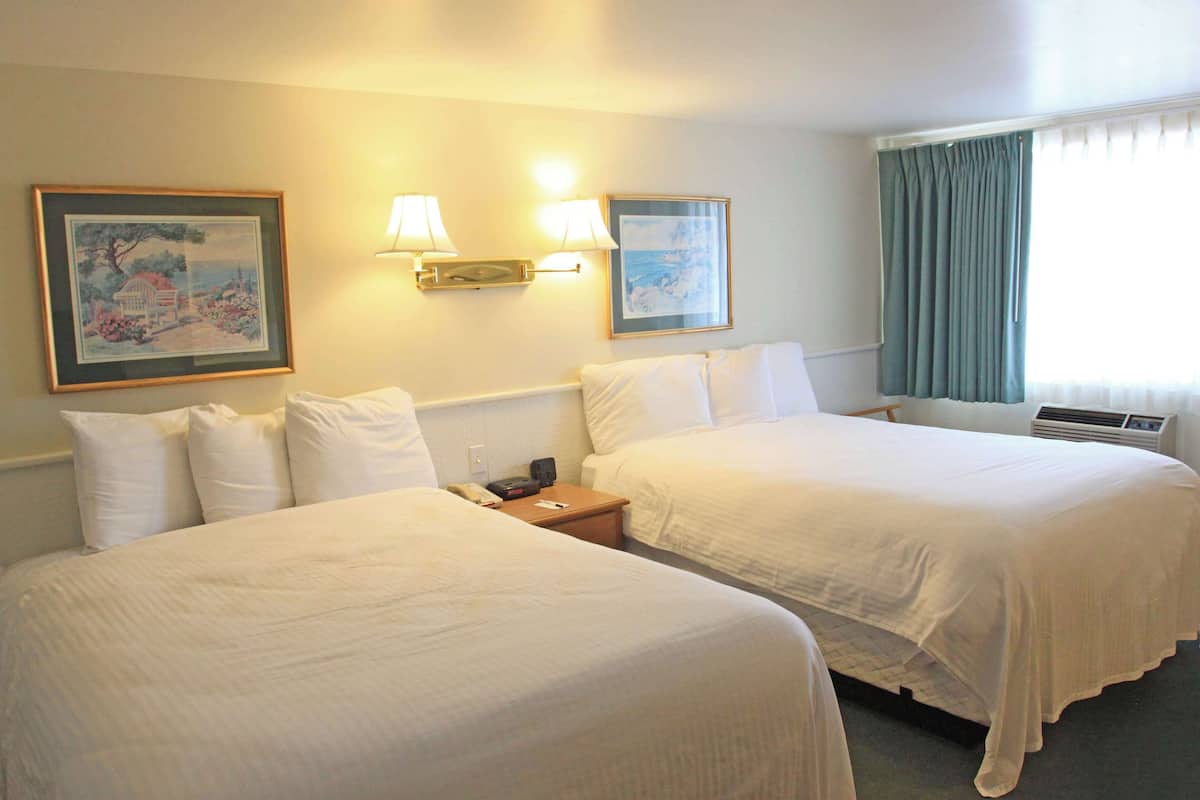 A hotel room with two beds, a nightstand, wall-mounted lamps, and framed artwork.