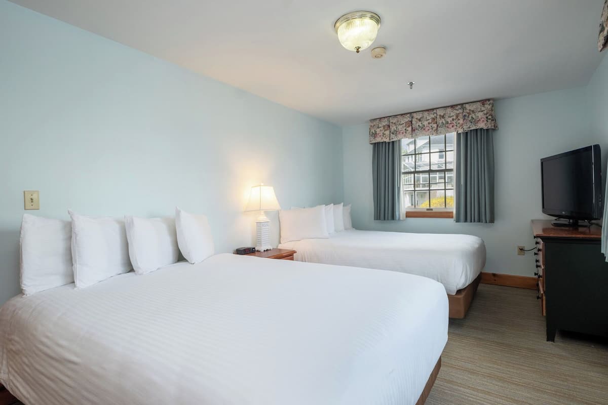 A hotel room with two beds, a television, a lamp, and a window with curtains.