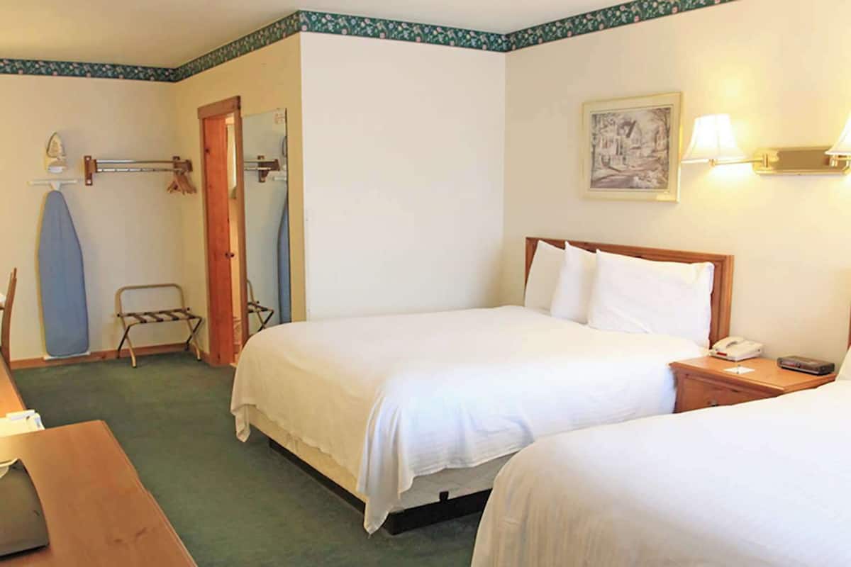 A hotel room with two beds, a wooden nightstand, a desk, and a chair.