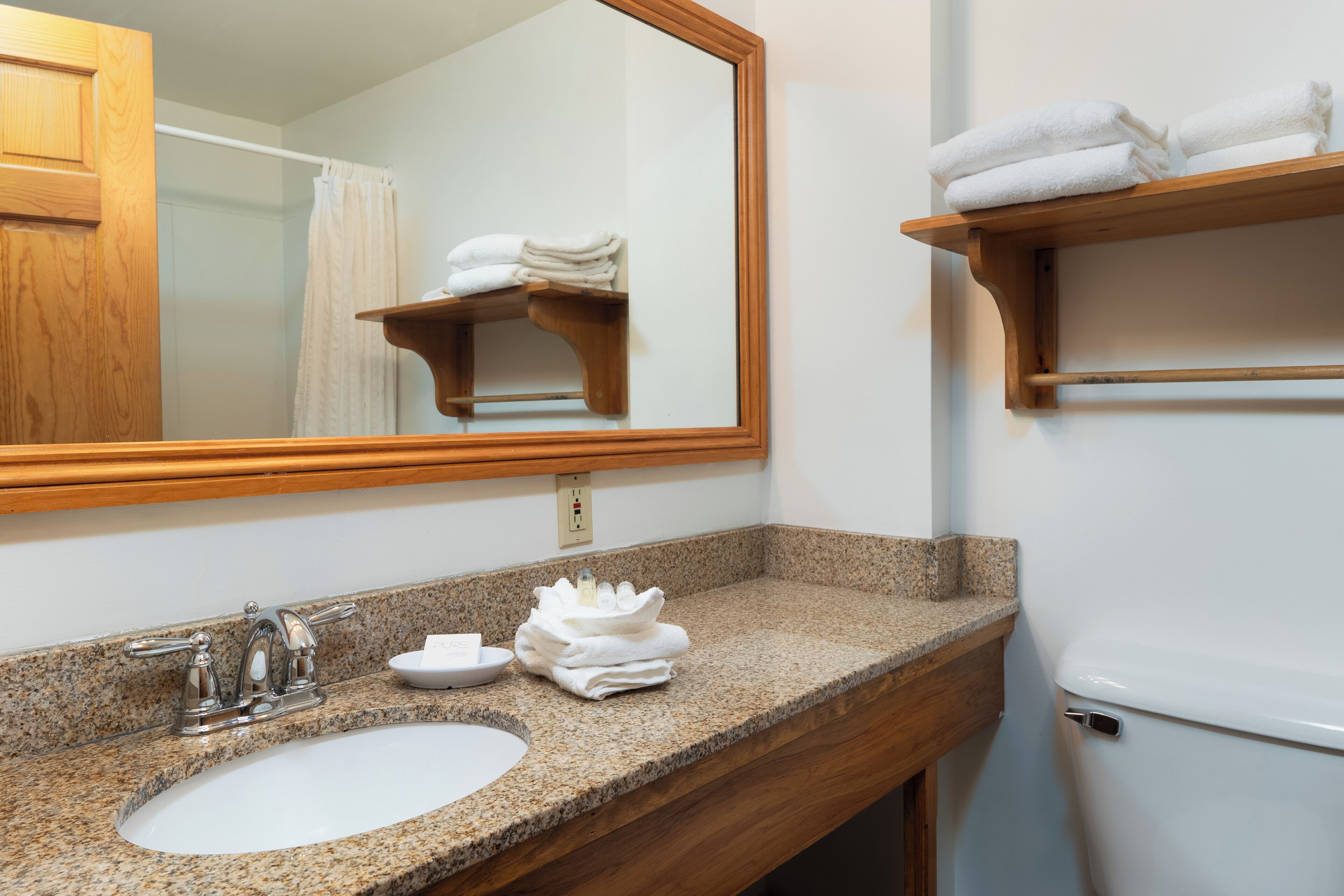 A bathroom with a granite countertop, a sink, a mirror, a towel rack, and a toilet.
