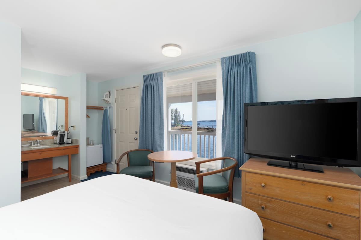 A hotel room with a bed, a TV, a desk with a chair, and a window with curtains.