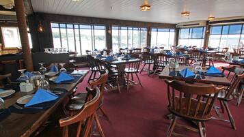 A restaurant with multiple tables and chairs, large windows, and a red carpeted floor.
