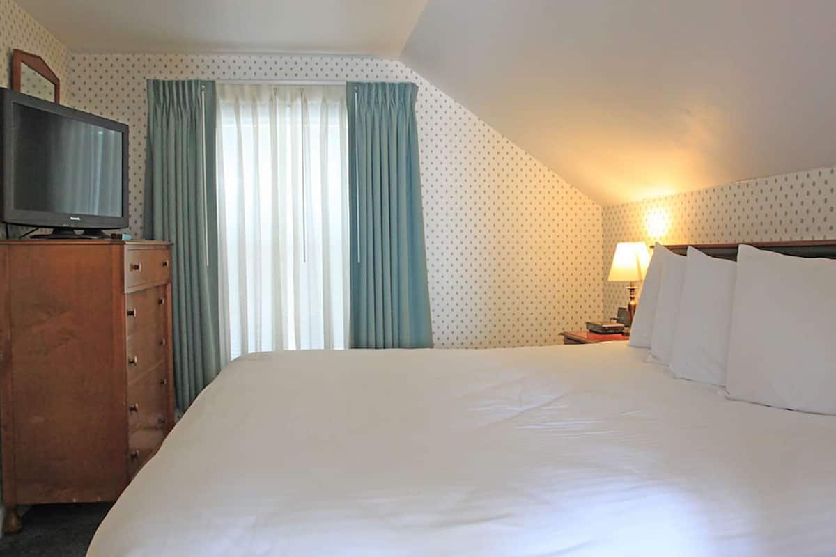 A hotel room with a large bed, a dresser, a television, and a window with curtains.