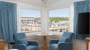 A room with two blue armchairs, a small wooden table, and a TV on the wall. - Tugboat Inn (Boothbay Harbor)