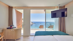 A hotel room with a bed, a desk, a TV, and a view of the sea. - Universal Hotel Aquamarin (Andraitx)