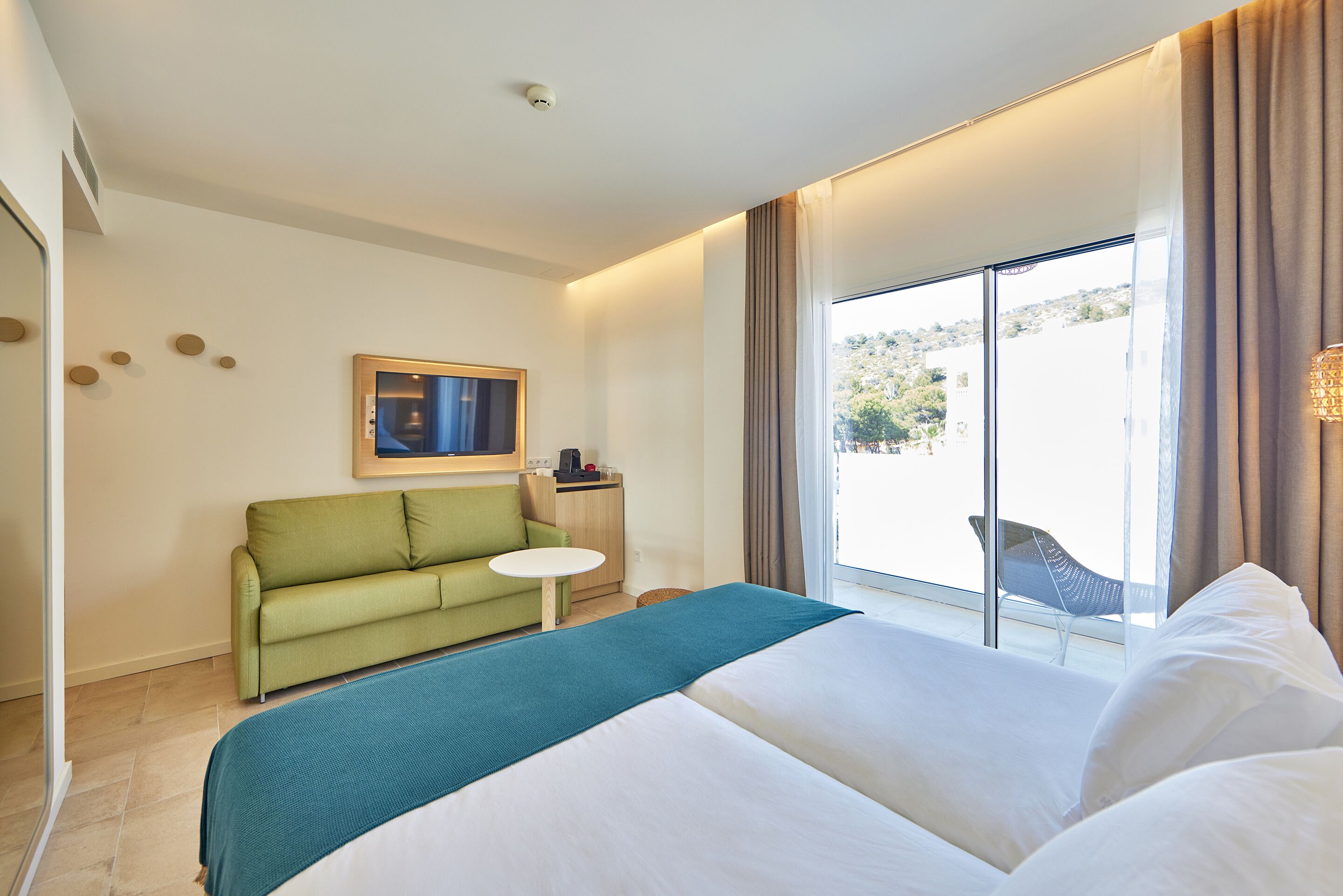 A hotel room with a bed, a green sofa, a small table, and a window with curtains.