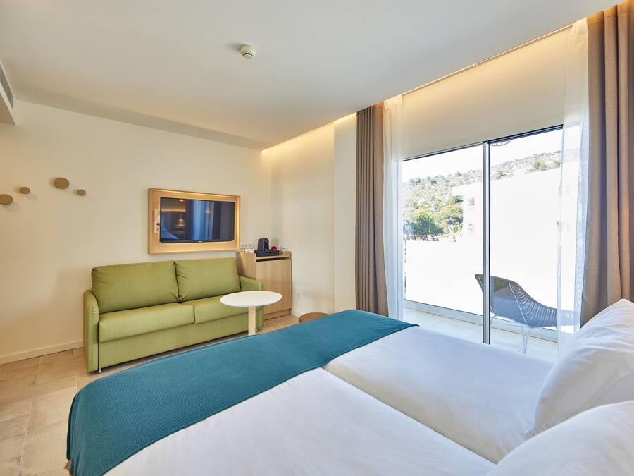 Una habitación de hotel con una cama, un sofá verde, una mesita y una ventana con cortinas.