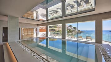 En modern inomhuspool med fin utsikt över havet och en balkong med solstolar.