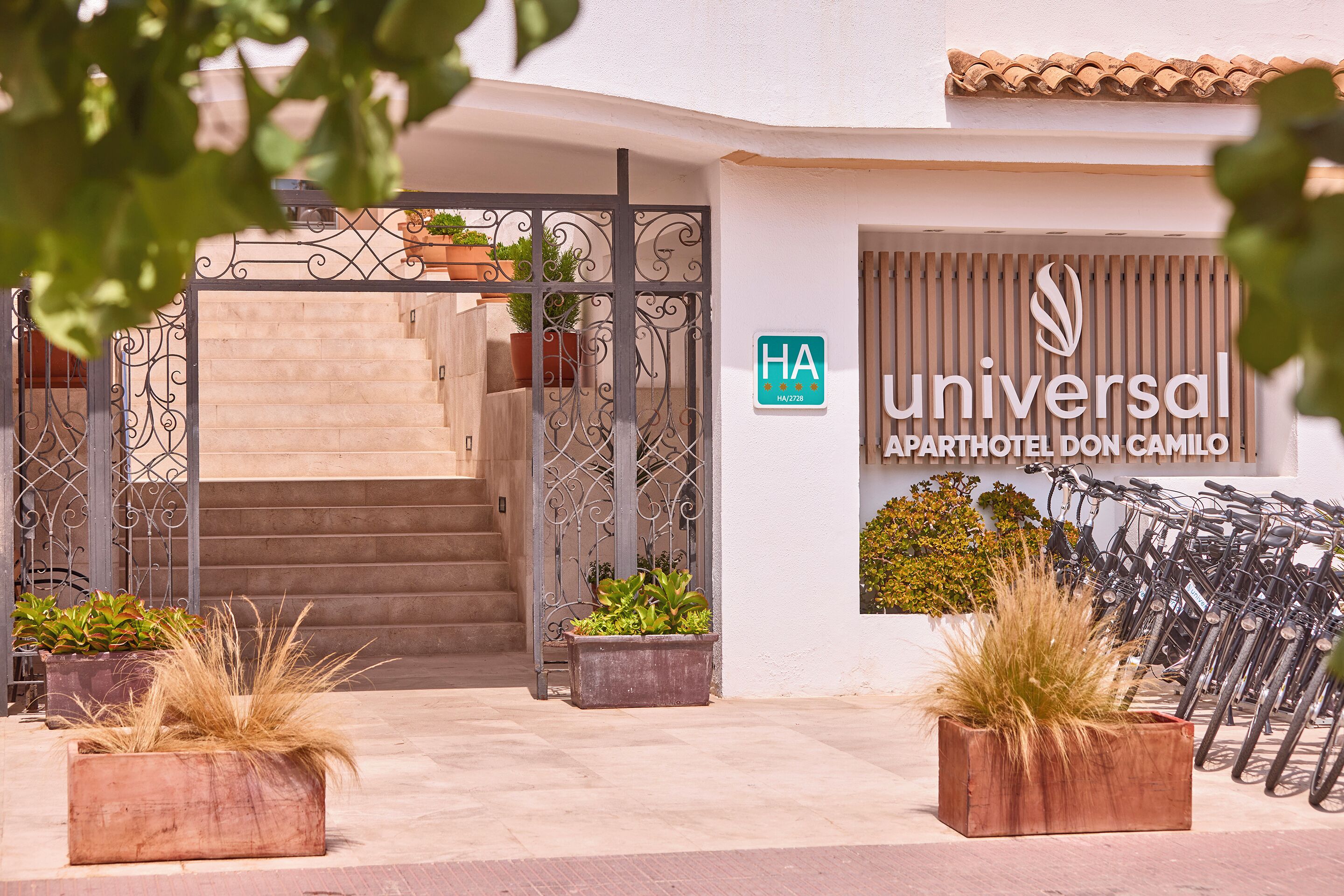 A hotel entrance with a wrought iron gate, potted plants, and bicycles parked outside.