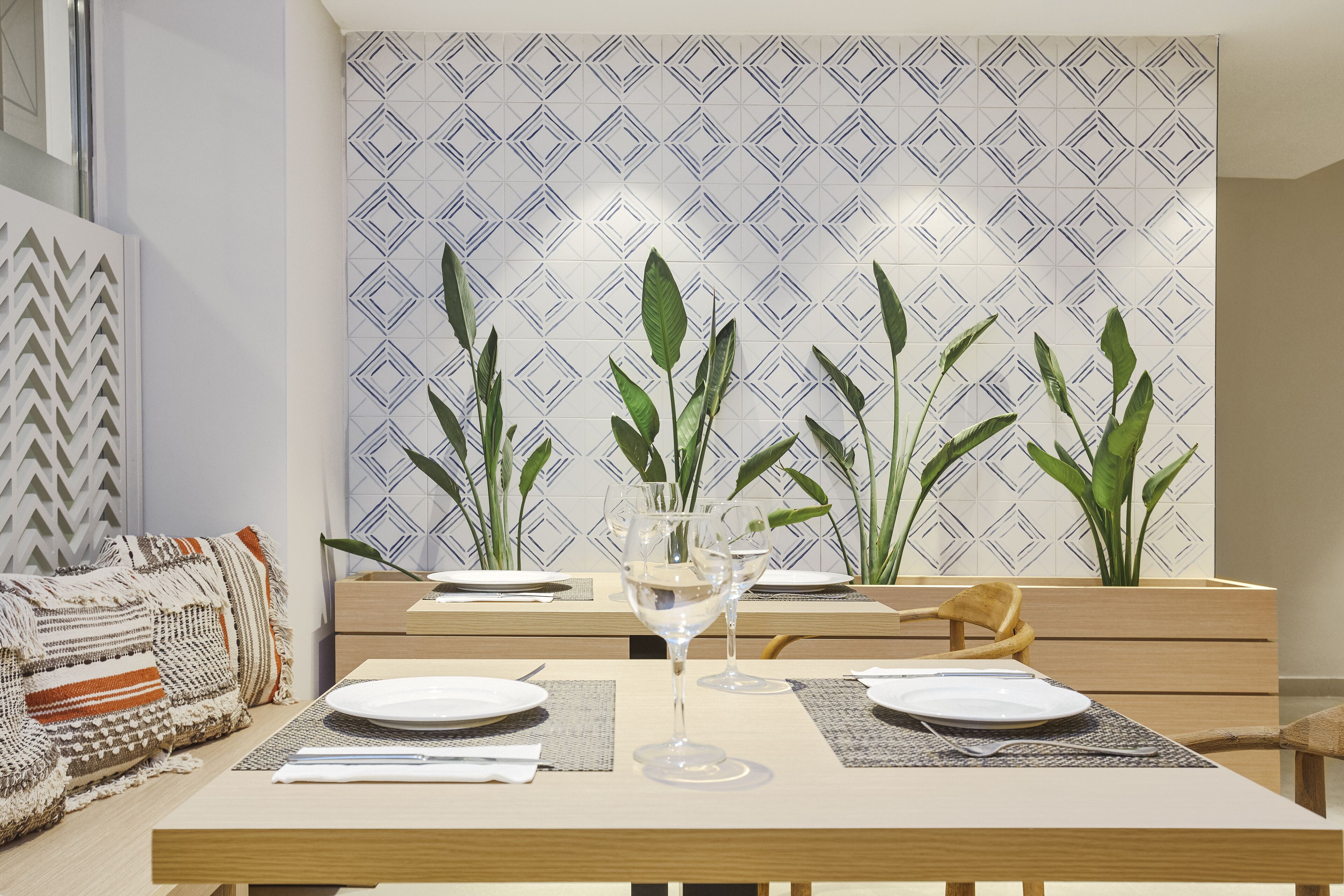 A dining area with a table set for two, two wine glasses, and a decorative plant in the background.
