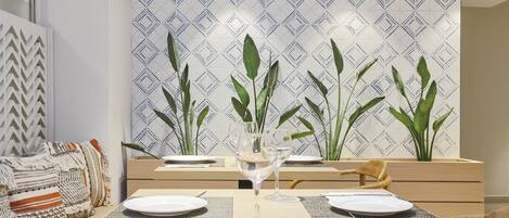 A dining area with a table set for two, two wine glasses, and a decorative plant in the background.