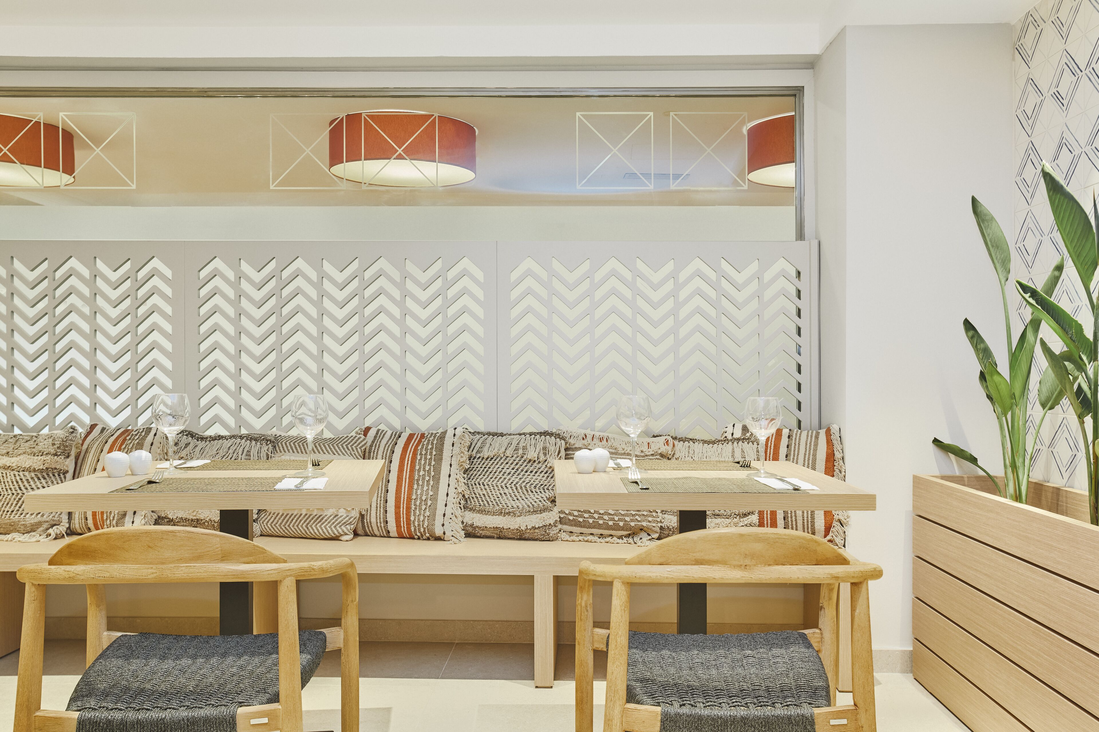 A modern dining area with a long wooden table, cushioned chairs, and a patterned wall behind the seating.