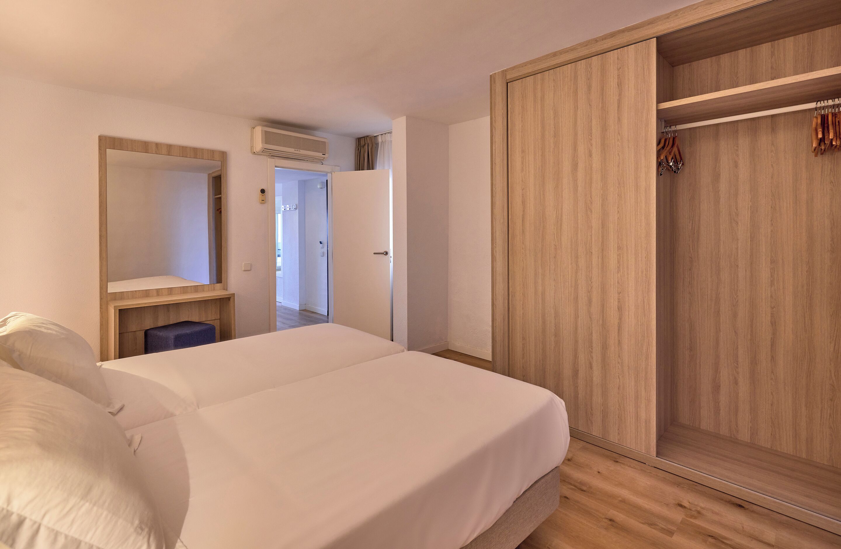 A bedroom with a bed, a wardrobe, a mirror, and a small table.