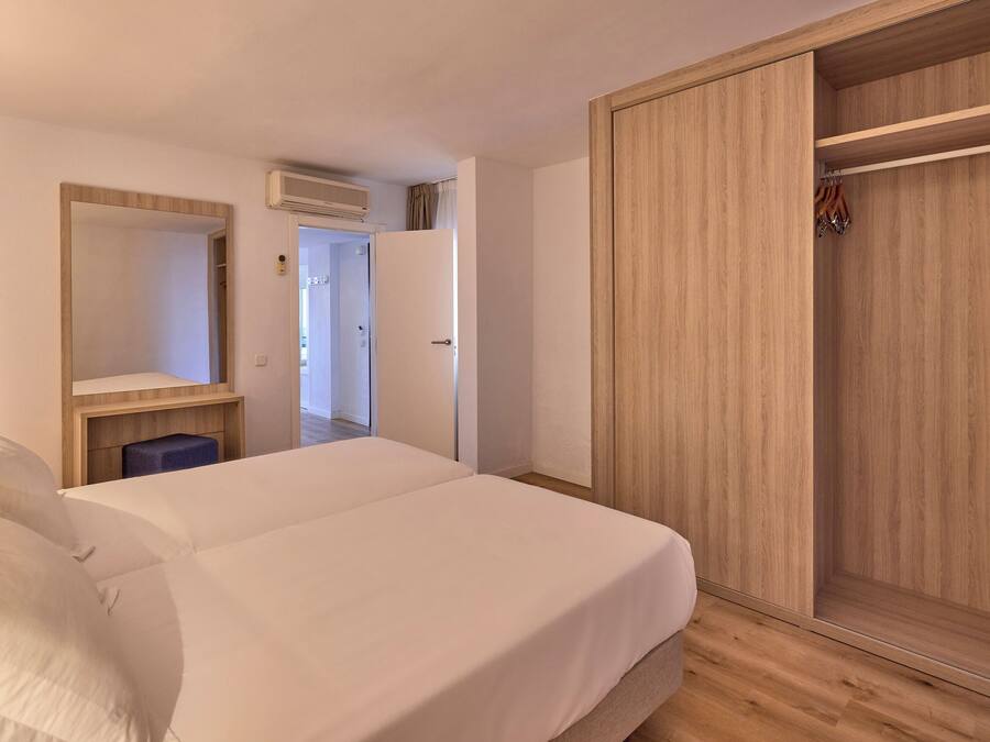 A bedroom with a bed, a wardrobe, a mirror, and a small table.