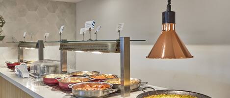 A buffet setup with various dishes and a large pan on a stove.