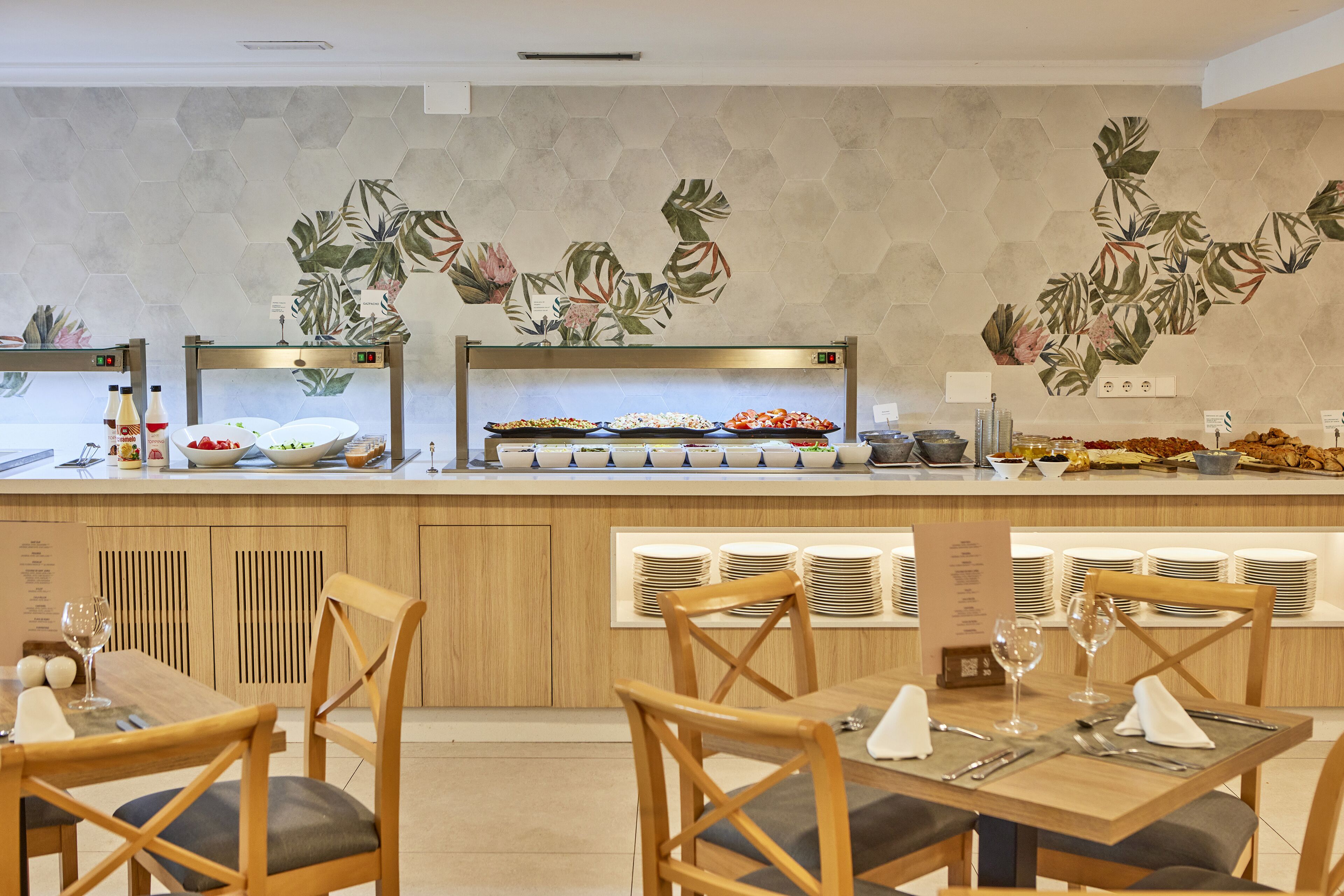 A buffet setup with various food items and a wall with a tropical leaf pattern.