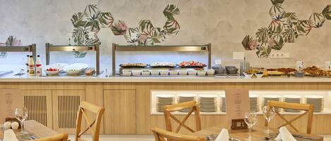 A buffet setup with various food items and a wall with a tropical leaf pattern.