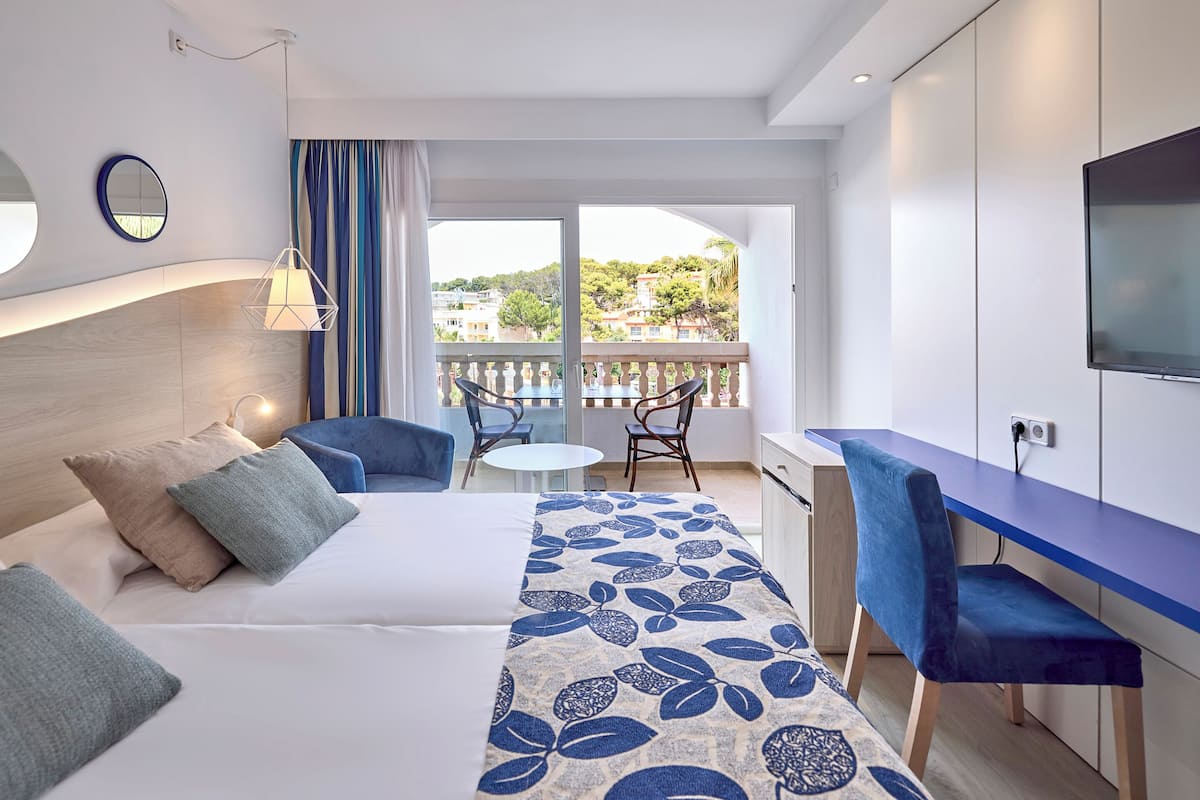 A modern hotel room with a bed, a desk, a chair, and a balcony with a view of the city.
