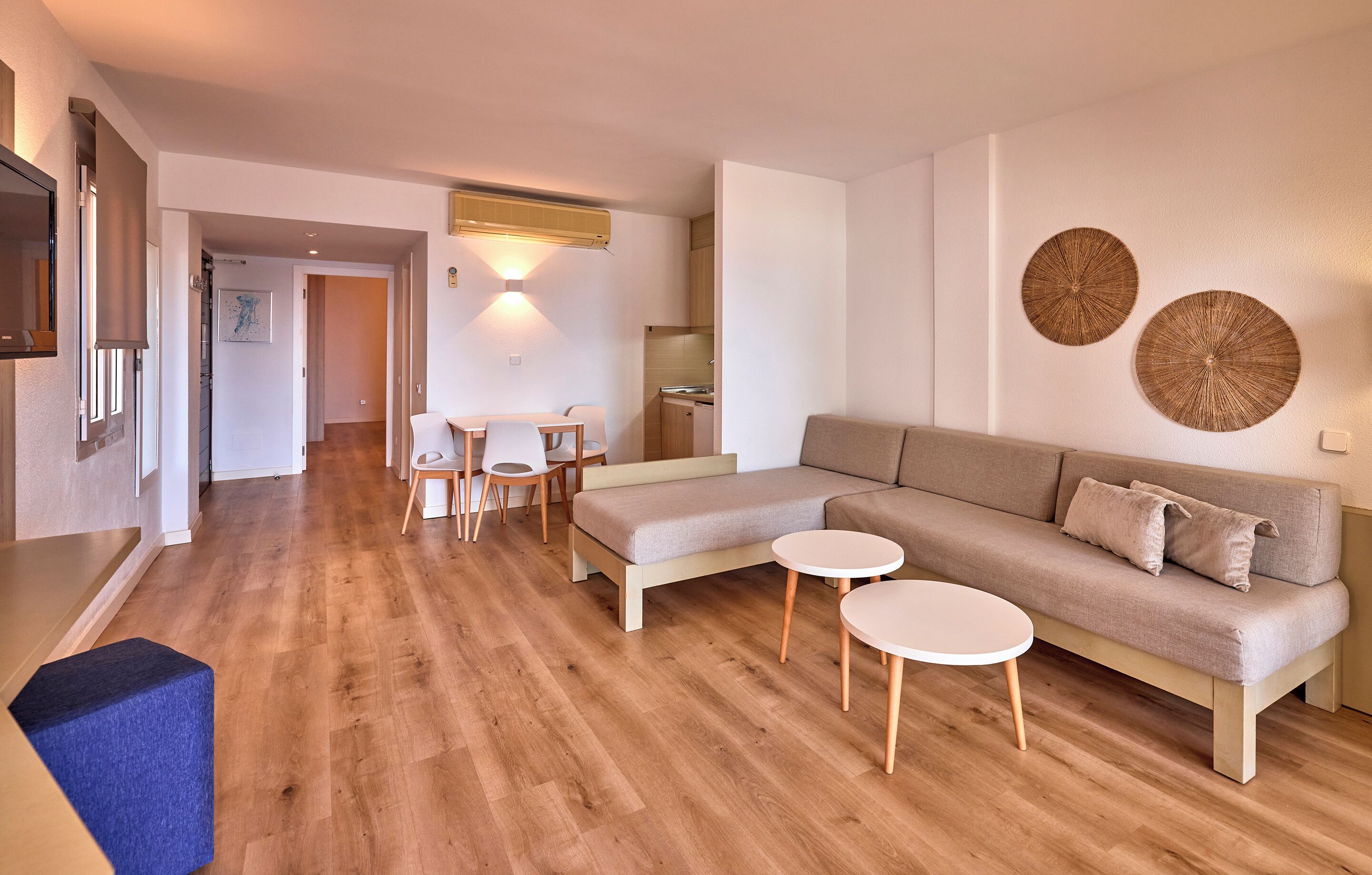 A modern living room with a sofa, two round coffee tables, a dining area with a table and chairs, and a kitchen in the background.