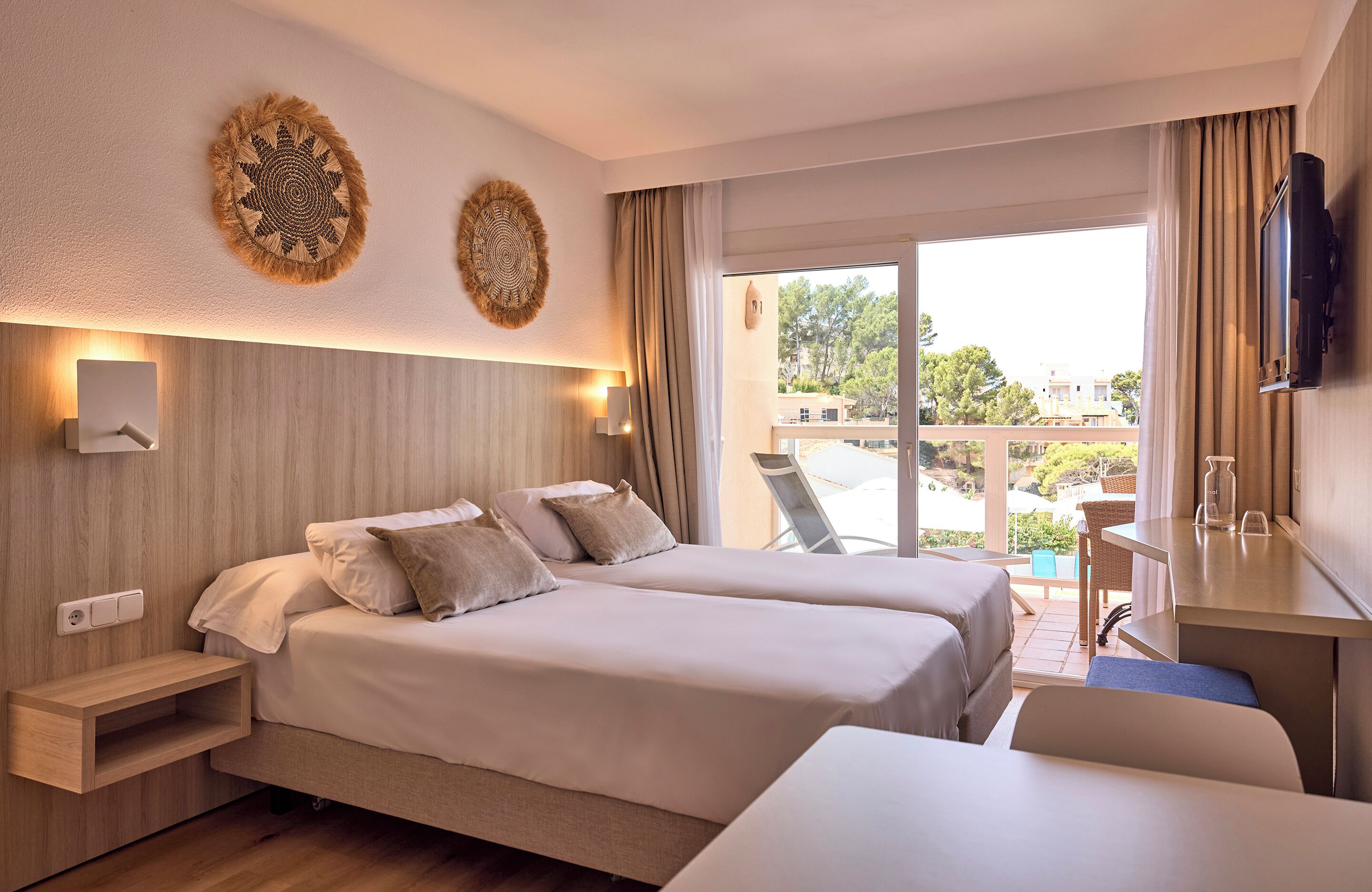 Habitación de hotel con dos camas, un escritorio, un televisor y un balcón con vista a la ciudad.