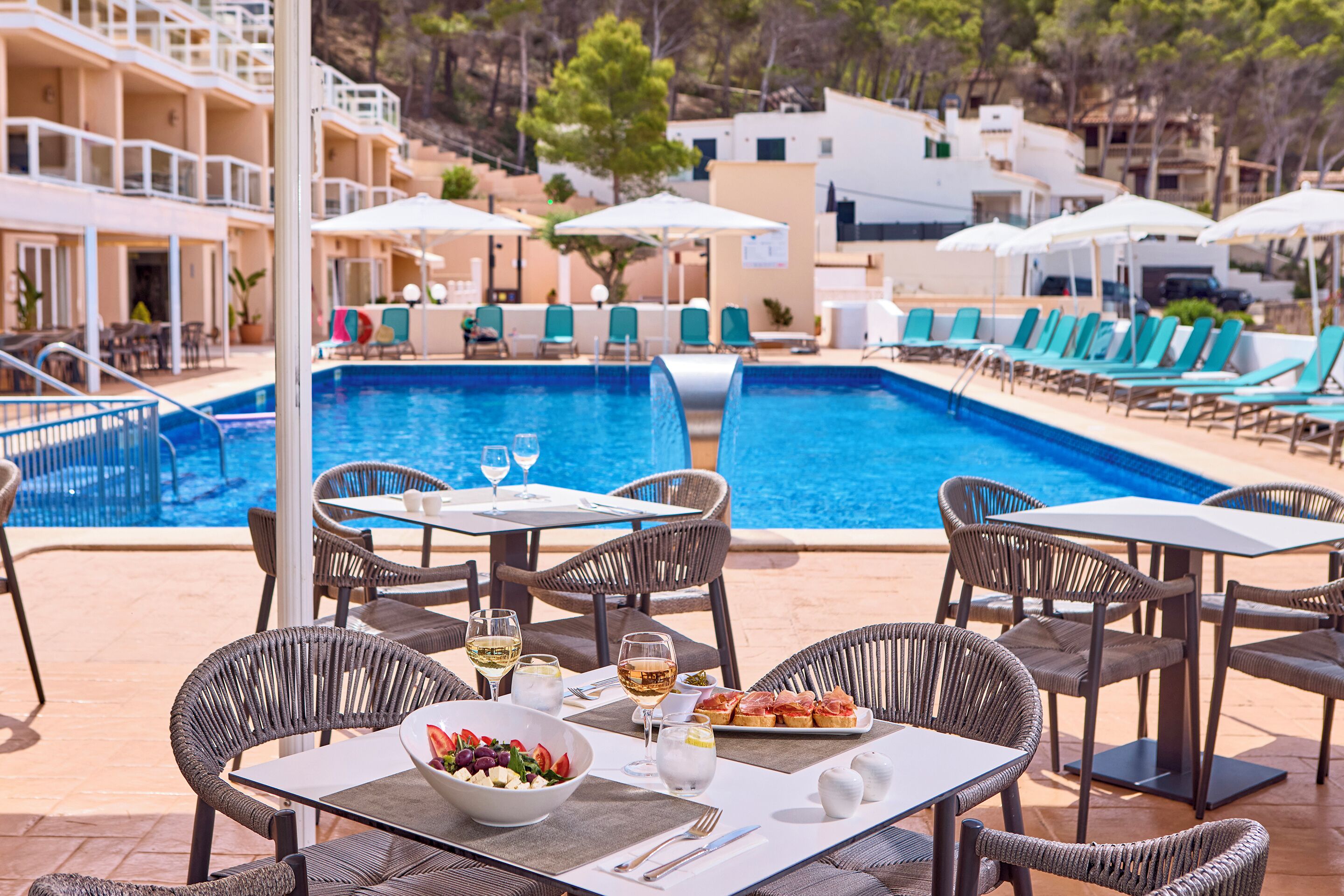 Area pranzo a bordo piscina con tavoli, sedie e vista sulla piscina.