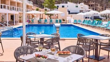 Un área de comedor junto a la piscina con mesas, sillas y vistas a ella.