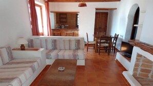 A living room with a sofa, a coffee table, a TV, and a fireplace. There is a kitchen in the background with wooden cabinets and a dining area with a table and chairs. - Benet Los Pinares Apartments (Santa Eulalia del Rio)