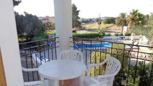 A balcony with a white table and chairs, a pool in the background, and a view of the surrounding area. - Benet Los Pinares Apartments (Santa Eulalia del Rio)