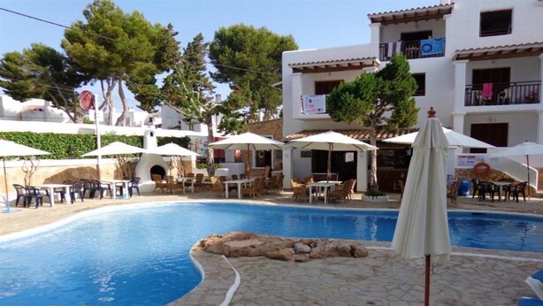 A pool area with lounge chairs and umbrellas, surrounded by a stone deck and a building with balconies. - Benet Los Pinares Apartments (Santa Eulalia del Rio)