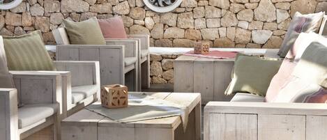 A stone wall with a rustic wooden seating area featuring cushioned chairs and a table.