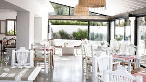Un comedor luminoso con mobiliario blanco y grandes ventanales con vistas a un jardín.