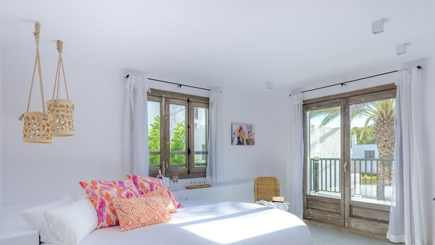 Un dormitorio luminoso con una cama grande, dos ventanas y un balcón.