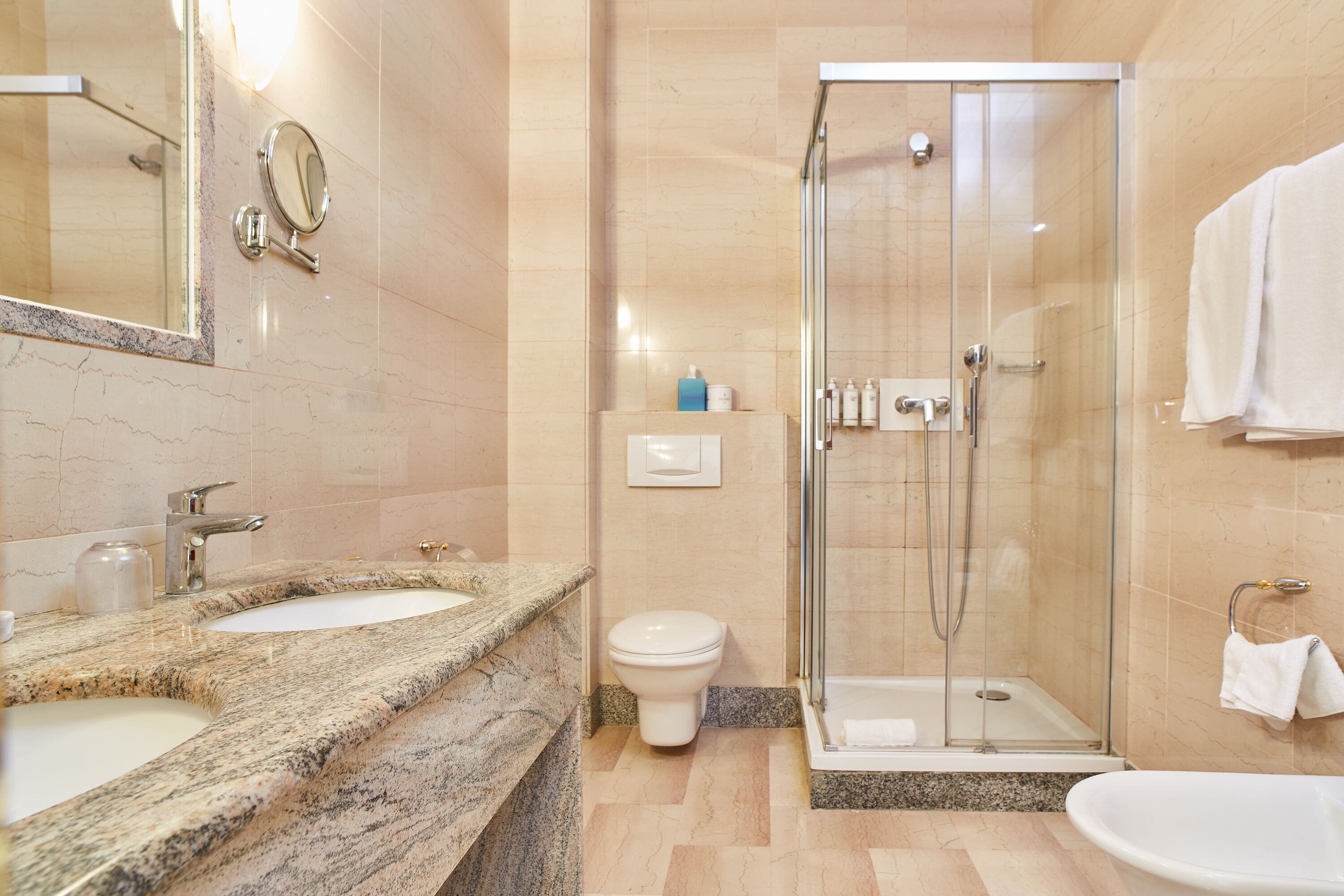 Ein modernes Badezimmer mit zwei Waschbecken, einer Toilette und einer gläsernen Dusche.