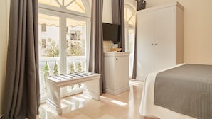 Un dormitorio con cama, un banco, un armario, un televisor y una ventana con cortinas.